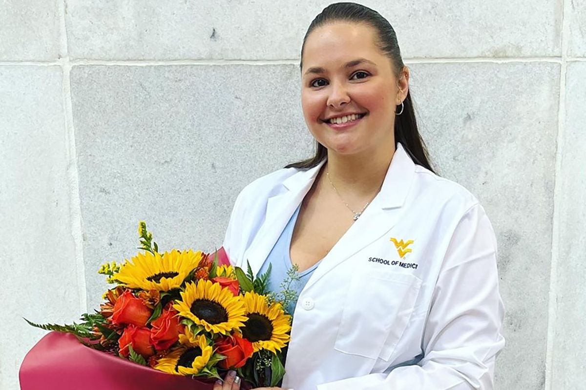 Photograph of Haley Link in a white lab coat holding a bouquet of sunflowers. 