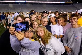 WVU President Gordon Gee and several students pose together for a selfie during an event at at the football stadium. 
