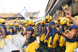 An image of WVU football players waiting to run onto the field for a previous football game. The many players in the photo are wearing blue jerseys, gold bottoms and gold helmets. 