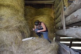 woman sits on hay in log structure using boring tools