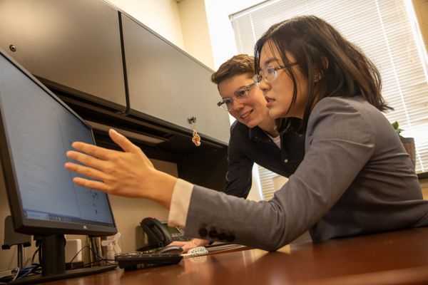 Two researchers are working together in an office discussing something on a computer screen. 