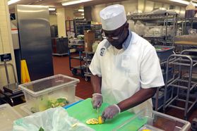 Man in white shirt, bill-less cap, latex gloves cuts lemons on green cutting board