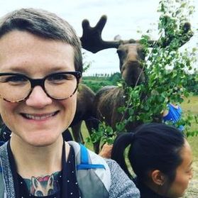 Woman with short hair and glasses smiles for a picture with a moose