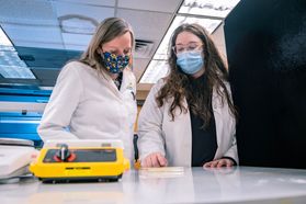 women in lab coats look at paper on counter