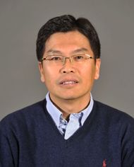 portrait of a man wearing glasses and v-necked blue sweater over light blue shirt