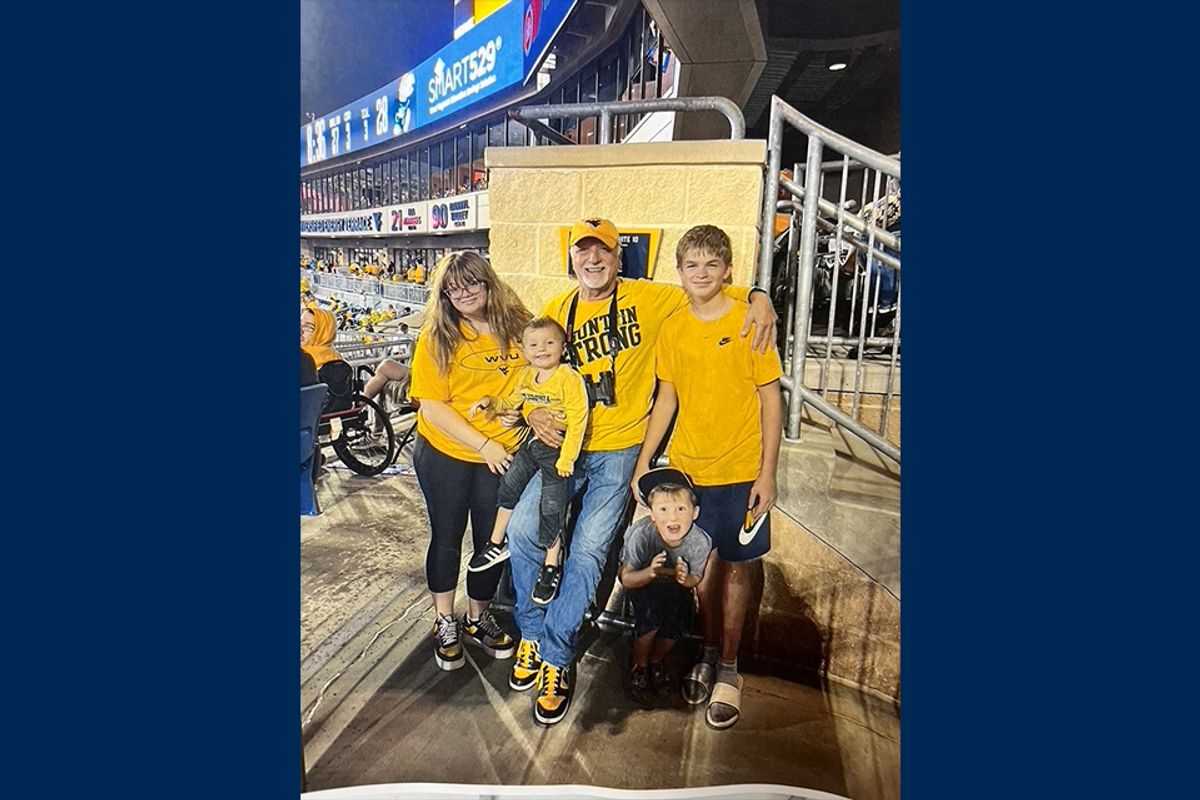 Dr. Philip High is shown surrounded by younger family members wearing gold shirts on game day at Milan Puskar Stadium.