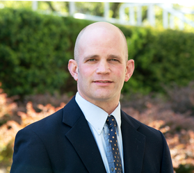 Jason Gross, an assistant professor in the Department of Mechanical and Aerospace Engineering, is pictured here wearing a dark suit and tie. 