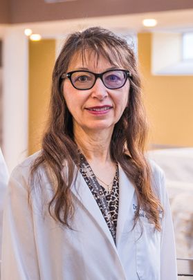 Headshot of WVU School of Dentistry professor R. Constance Wiener. She is pictured in her white lab coat with an animal print shirt underneath. She has long, light brown hair and is wearing black framed glasses. 