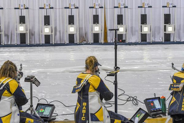 Three blonde women in WVU rifle team uniforms shoot at targets 