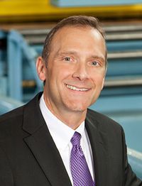 Retired president and CEO of Eagle Manufacturing poses for a headshot wearing a black suit with a purple tie. His light-colored hair is cut short.