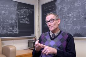 man in glasses in front of chalkboards