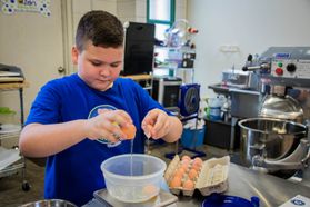 A boy in a blue t-shirt cracks eggs into a container