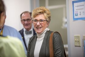 blonde woman with glasses smiles at people, man in background