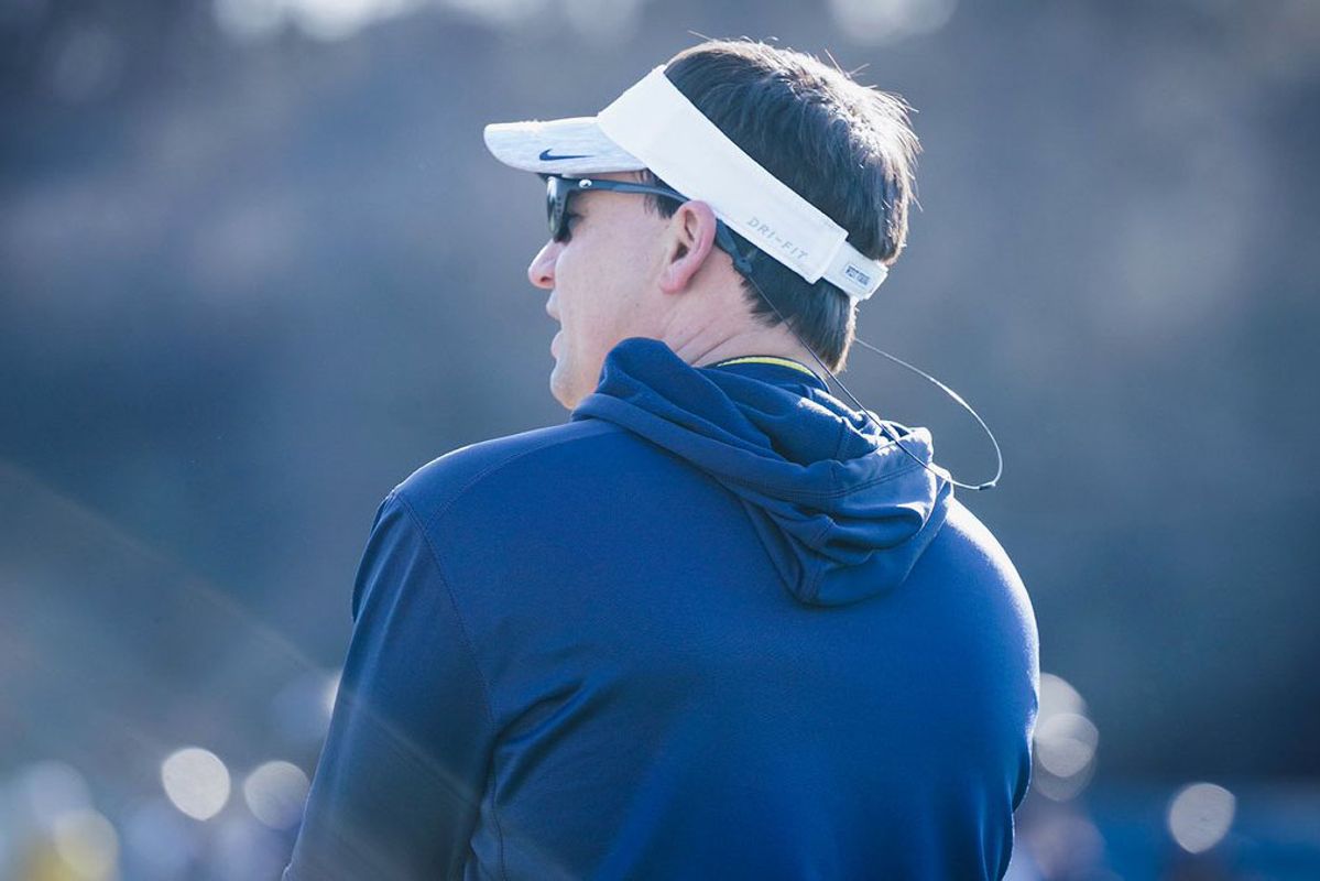 WVU football coach Neal Brown oversees practice in a white visor and blue hoodie.