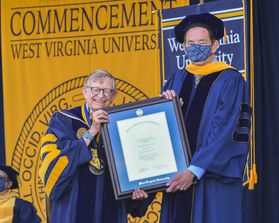 men in graduation regalia hold a framed certificate