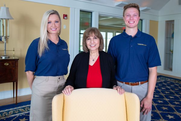Two women and a man stand behind a yellow chair