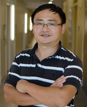 Headshot of a WVU professor Cangliang Shen. He is pictured inside wearing a dark shirt with white stripes. He is standing with his arms crossed and is wearing glasses. He has short black hair. 