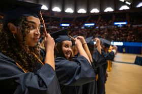 Several graduates wearing navy blue caps and gowns move their tassels to the left at the Coliseum.