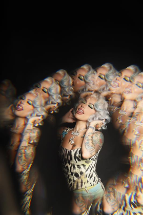 A person with gray hair, heavy eye makeup, wearing a leopard body suit is in the center of this photo. A special effect circles the person with a kaleidoscope-type image of themselves.