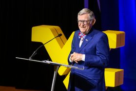 President Gordon Gee smiles during his spring State of the University address. He is standing at a clear podium and is wearing a blue suit.