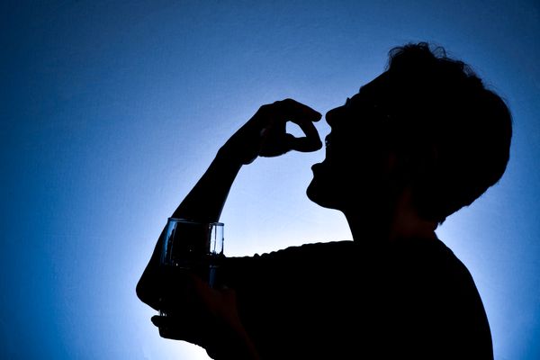 silhouette of woman putting pill in her mouth; holding glass of water