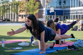 Female students practice yoga on the West Virginia University campus. The Mountainlair can be seen in the background of the photo. 