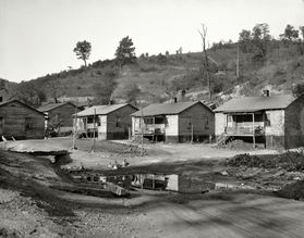 black and white photo of a row of small houses with a nearly-bare hillside in the background