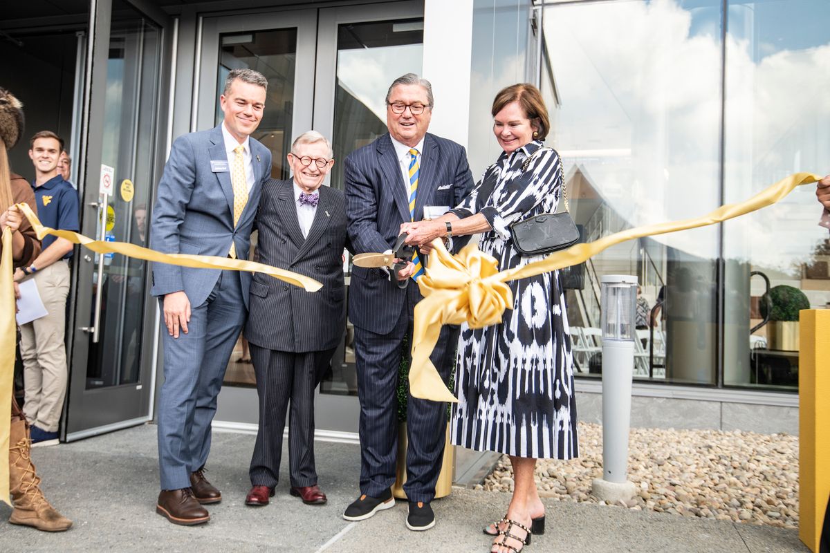 Four people are in the photo cutting a yellow ribbon in front of a building — Josh Hall, Gordon Gee, Bob Reynolds, Laura Reynolds