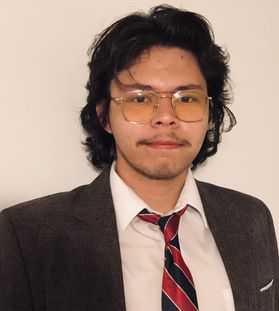 Headshot of scholarship recipient Nathanial Dunbar. He is pictured against a light colored background and is wearing a dark colored jacket over a white dress shirt and a black and red striped tie. He has shoulder length dark hair and wears glasses. 