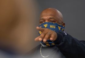 A teacher in a gold and blue WVU face covering points at a student