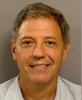 Headshot of WVU professor Sergio Caporali-Filho. He is pictured against a beige background and is wearing a gray striped shirt. He has short graying hair. 