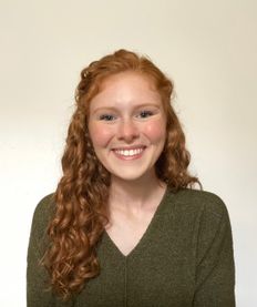 Scholarship recipient Erinn Victory is pictured here. She has long, curly red hair and is wearing a V-neck, olive green sweater.