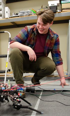 A student works on a robot connected to multi-colored wires.