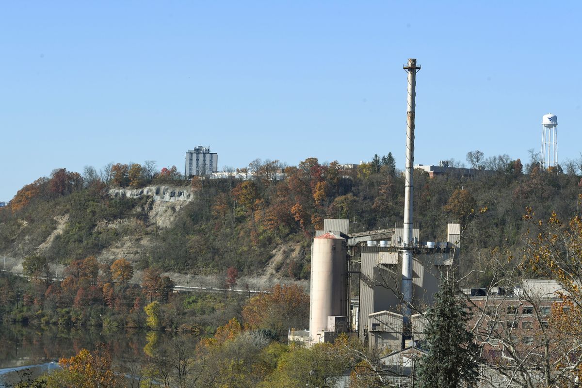 large steam plant with steep hillside, tall building in background