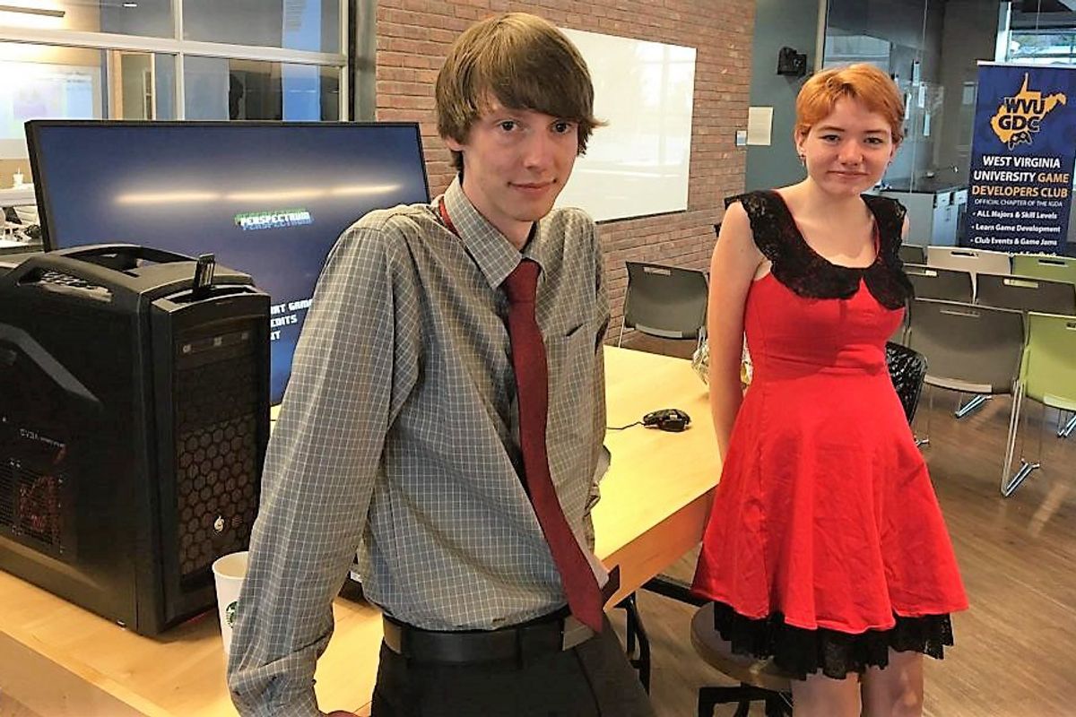 Man standing in gray shirt and red tie in front of desk with girl wearing red and black dress with strawberry blonde hair