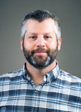 man in plaid shirt, dark hair, graying beard