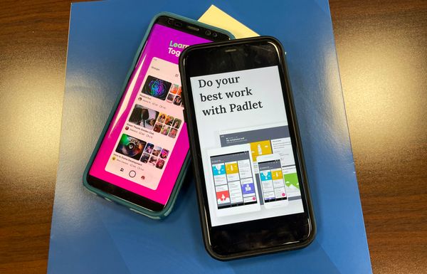 An image of two phones on top of a blue paper on top of a wood desk. One phone is laying on top of the other slightly. Each phone displays the landing page of an educational app. 