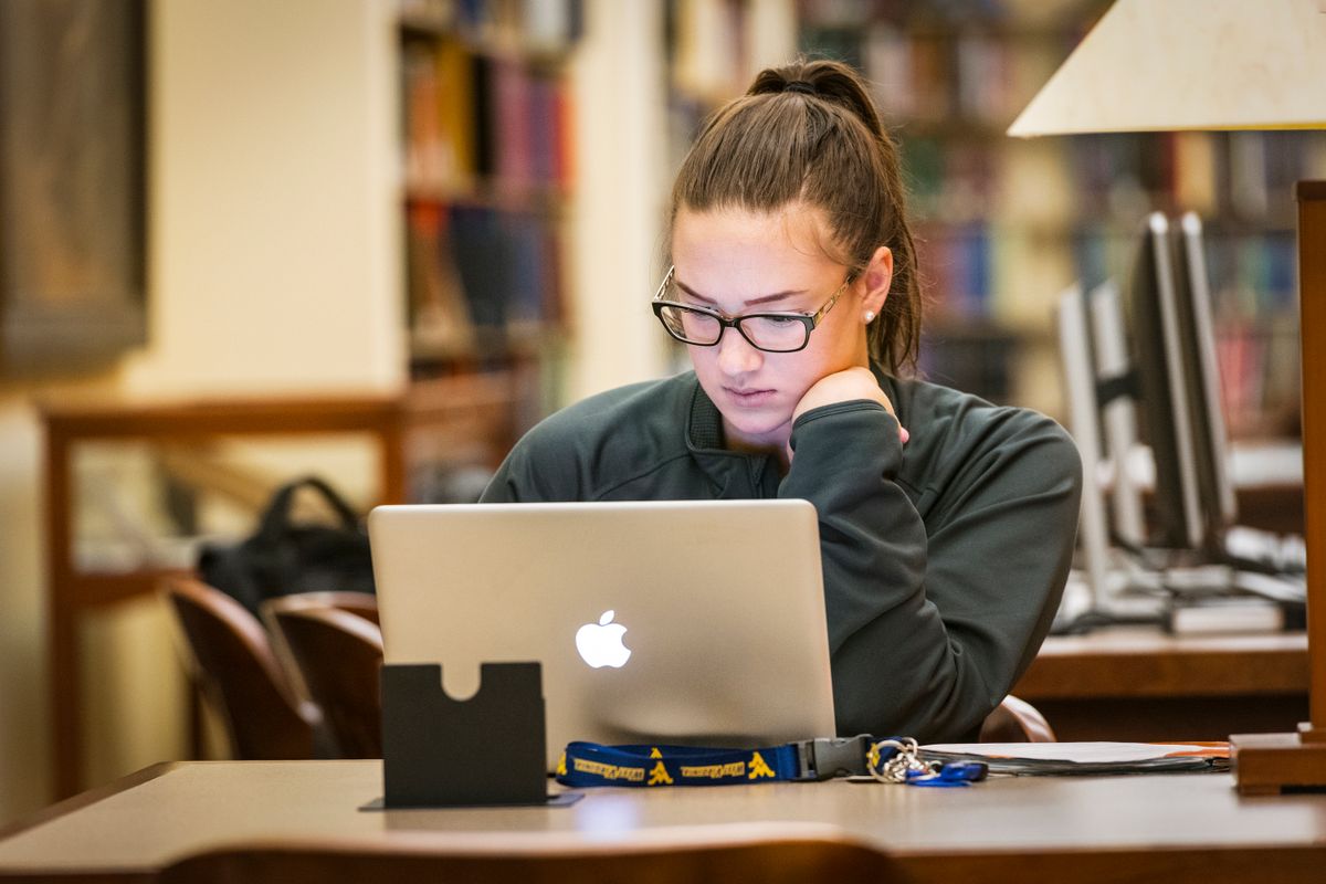 a young woman sits in a library using a laptop computer