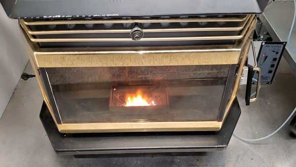 The camera is pointed down looking into the inside of a pellet stove. A small fire can be seen behind glass. The stove is edged in gold.