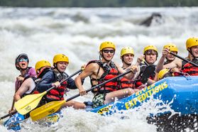 A group of eight WVU students on a First-Year Trip brave the rapids of the New River in a bright blue raft. 