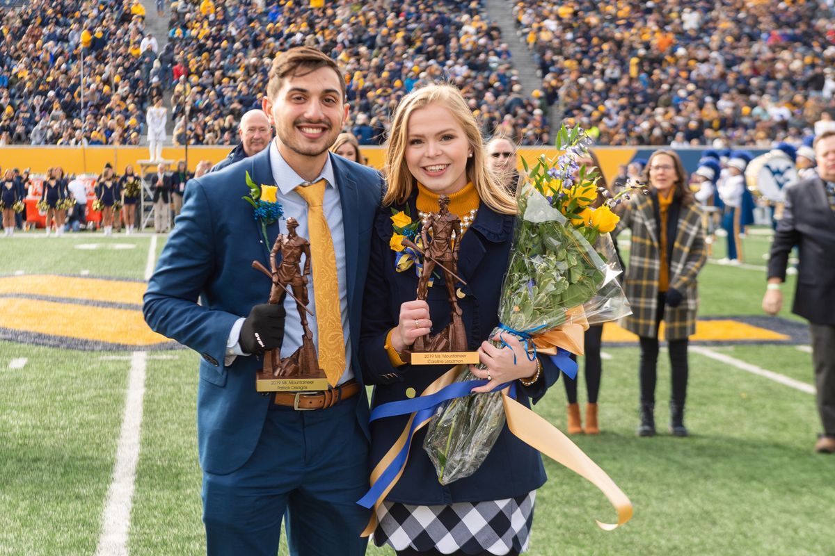 man and woman stand on a football field with flowers and small statues