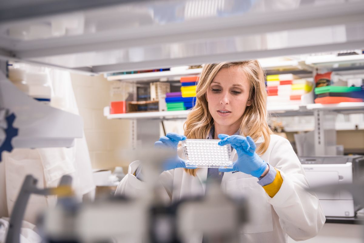 blonde woman in whitecoat, blue gloves in laboratory