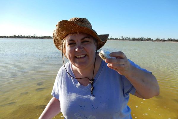 Woman in blue shirt and brown hat stands in a yellow and green body of water, holding up a white sea creature