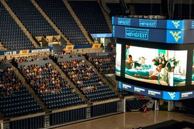 A large crowd of students sitting in the coliseum as a movie plays on the large screens