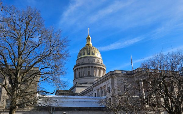 The golden dome of the West Virginia capitol building towering above trees and contrasting with the bright sky.