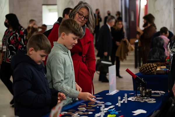 Three kids and adult pick up stickers from a display table set up in the State Capitol rotunda for WVU Day at the Legislature.