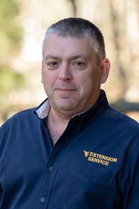 Headshot of WVU Jackson's Mill Director David Snively. He is pictured outside wearing a navy blue button up shirt that says WVU Extension Service on the breast pocket. He has short salt and pepper hair. 