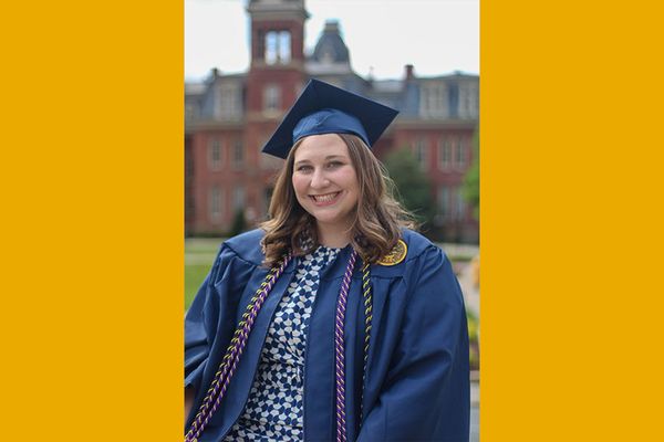 Headshot of WVU accounting student Claire Ullom dressed in her navy blue WVU Commencement regalia. Woodburn Hall can be seen in the background. 