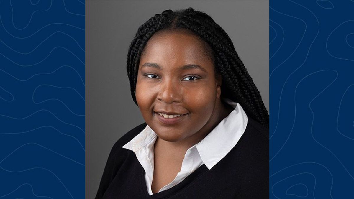 Headshot of WVU alumni Krystal Capers. She is pictured in front of a gray background wearing a black sweater over a white collared shirt. She wears her dark colored hair in braids. 