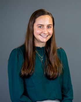 Headshot of WVU student Megan Weaver. She is pictured against a gray background wearing an emerald green blouse. She has long brown hair. 